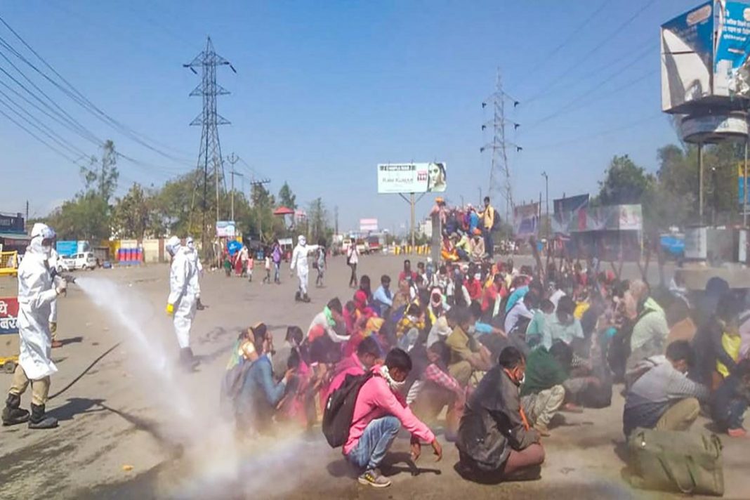 Trabalhadores indianos são forçados a permanecer no chão enquanto são pulverizados com desinfetantes usados ​​em ônibus